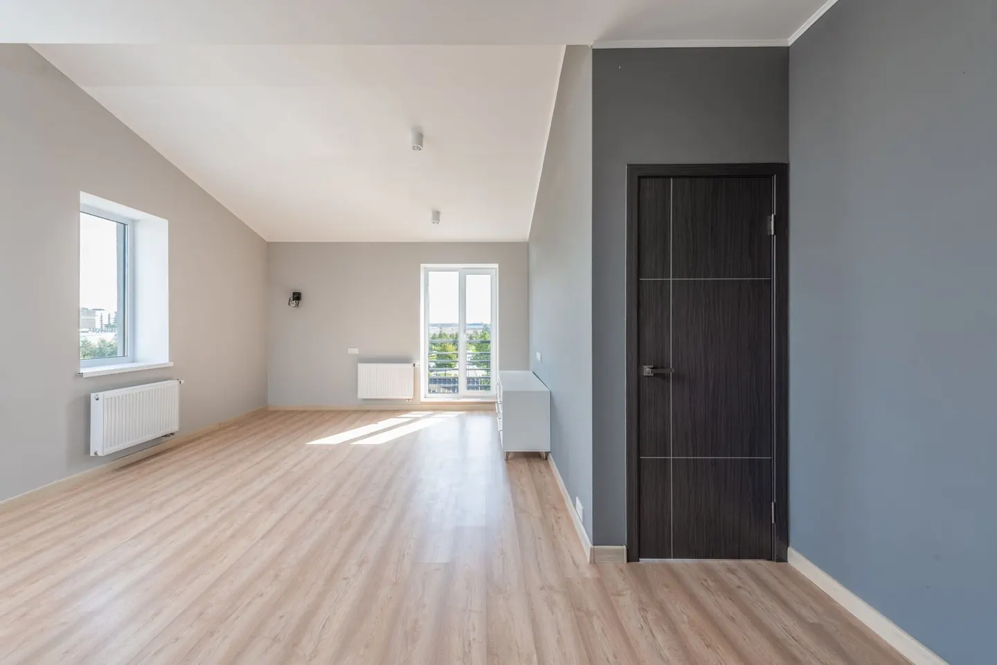 Pièce vide aux murs clairs, avec un parquet et des fenêtres laissant entrer le soleil